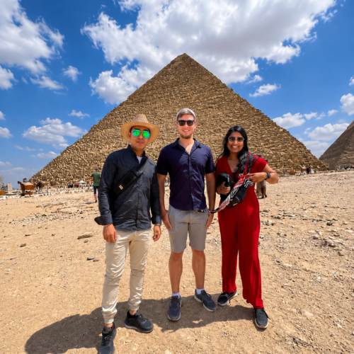 Tourists enjoying a camel ride in front of the Great Pyramids of Giza during a private half-day tour with an authentic Egyptian lunch."