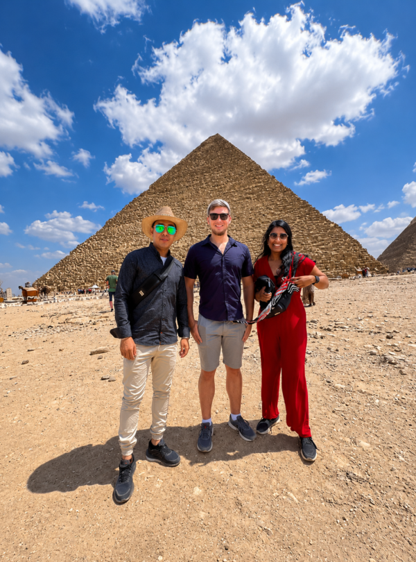 Tourists enjoying a camel ride in front of the Great Pyramids of Giza during a private half-day tour with an authentic Egyptian lunch."
