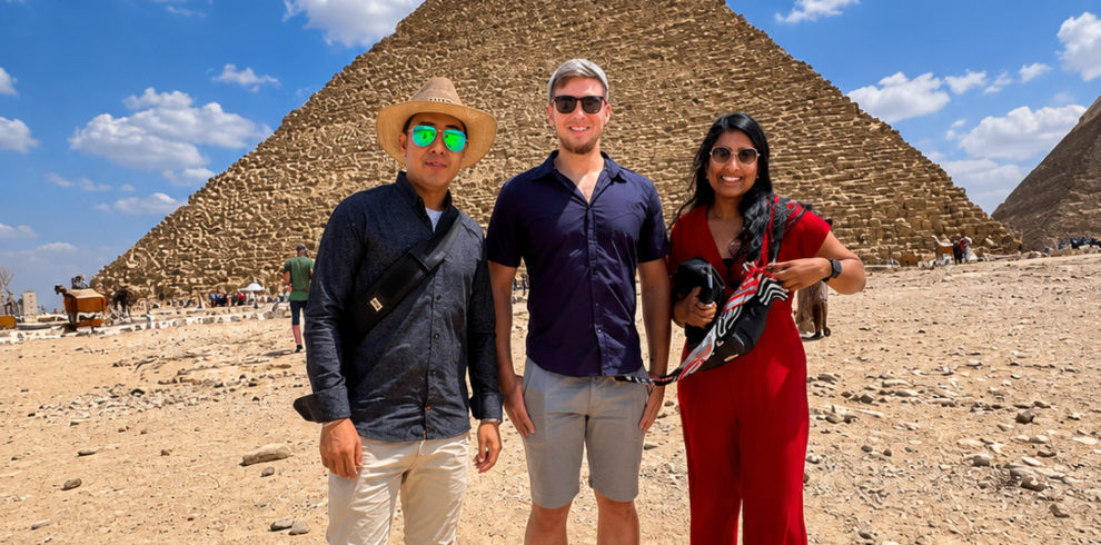 Tourists enjoying a camel ride in front of the Great Pyramids of Giza during a private half-day tour with an authentic Egyptian lunch."