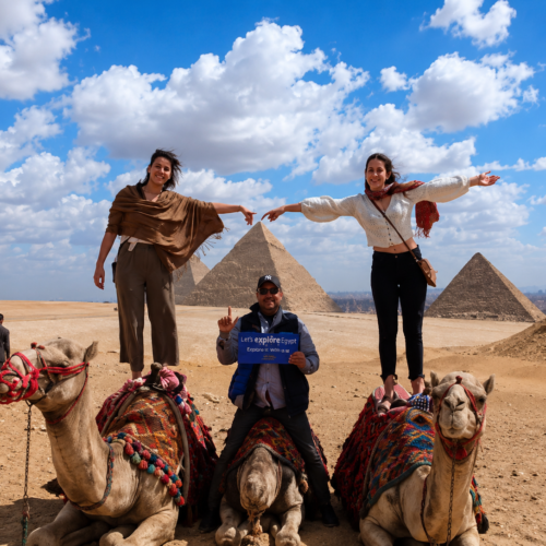 Tourists enjoying a camel ride in front of the Great Pyramids of Giza during a private half-day tour with an authentic Egyptian lunch."